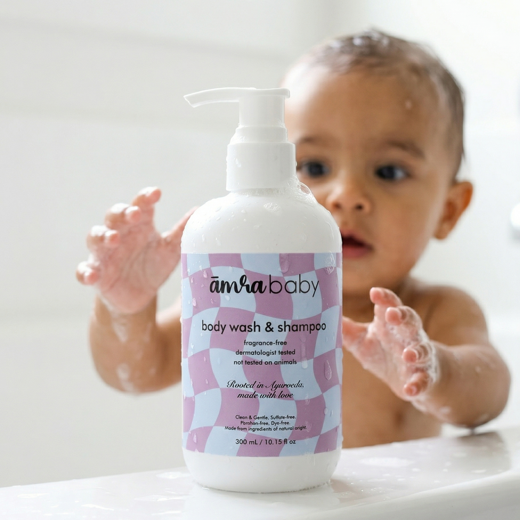Happy infant reaching for a bottle of Amra Baby fragrance free body wash & shampoo during bath time