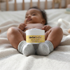 Infant resting on a textured blanket with a jar of Amra Baby Body Balm between their feet